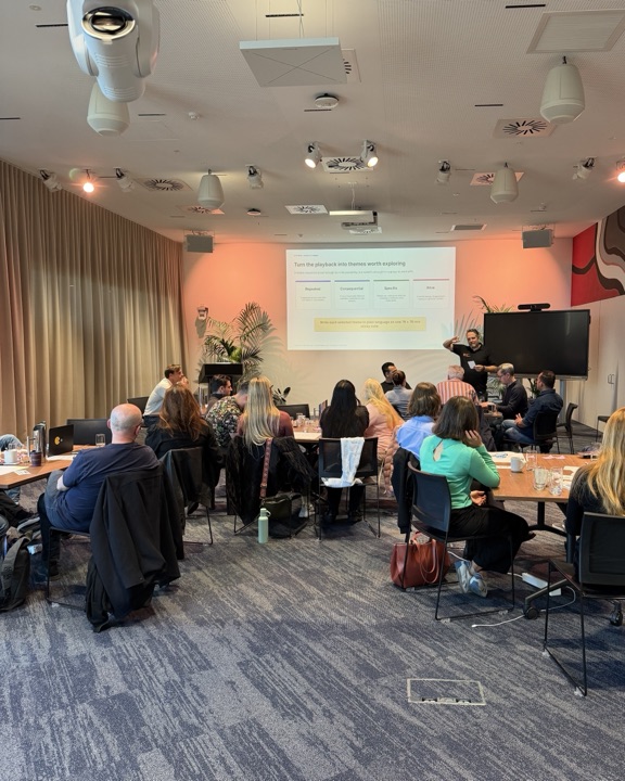 A speaker addressing seated participants beneath a slide about themes worth exploring.