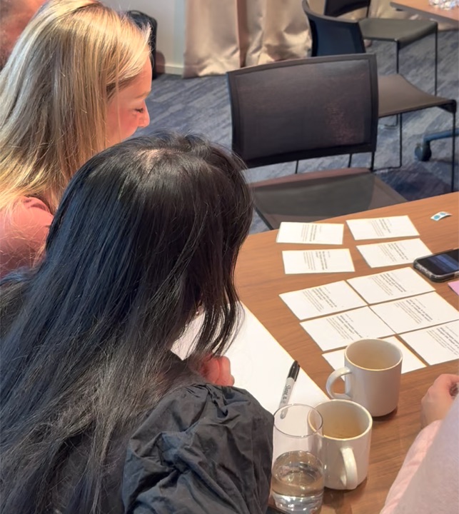 Participants reading printed prompts beside notebooks and coffee cups.